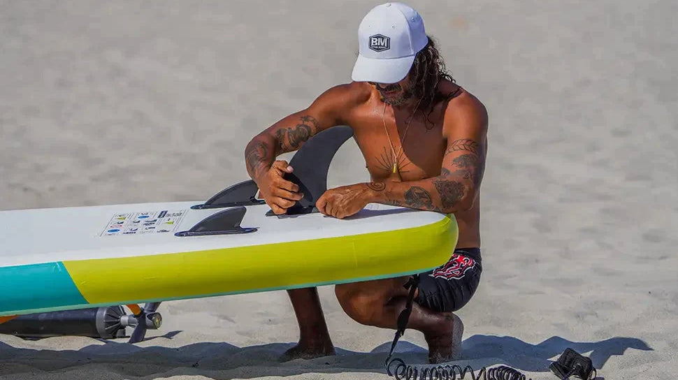 Man sitting on beach with surfboard, choosing tail fins for SUP