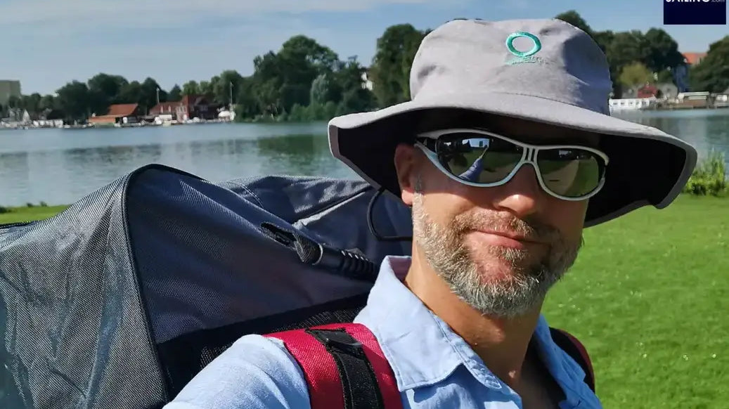 Man with backpack and sunglasses taking a selfie while stand-up paddleboarding adventure.