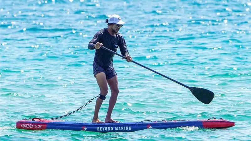 Man in long-sleeved shirt and shorts paddleboarding on colorful inflatable racing SUP