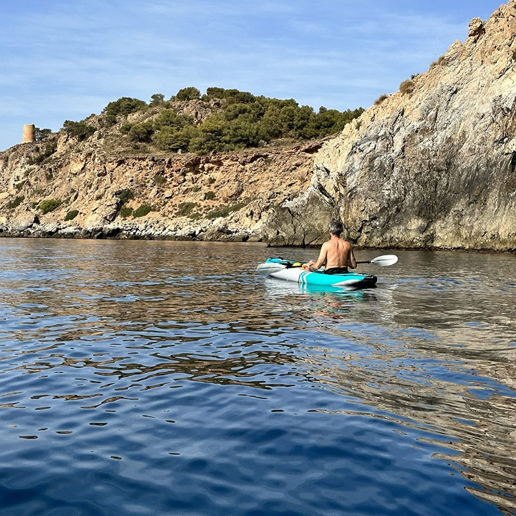 Person kayaking in calm water with a rocky cliff and greenery in the background