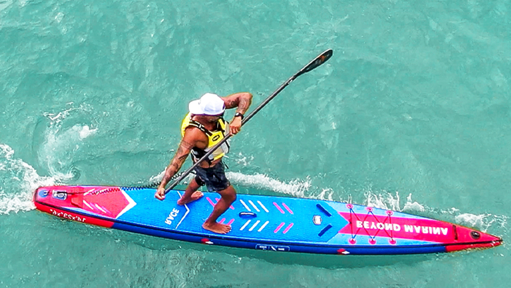 Person paddleboarding on a blue and red board in clear water