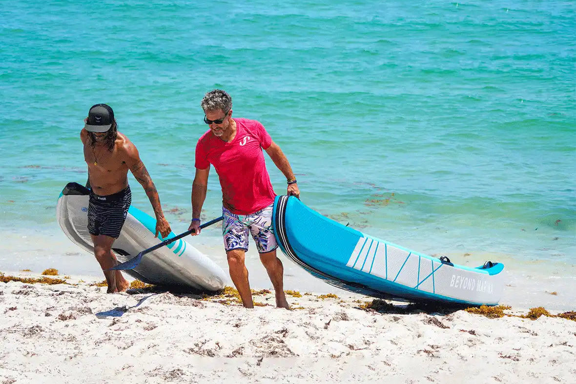Two people carrying inflatable kayaks.