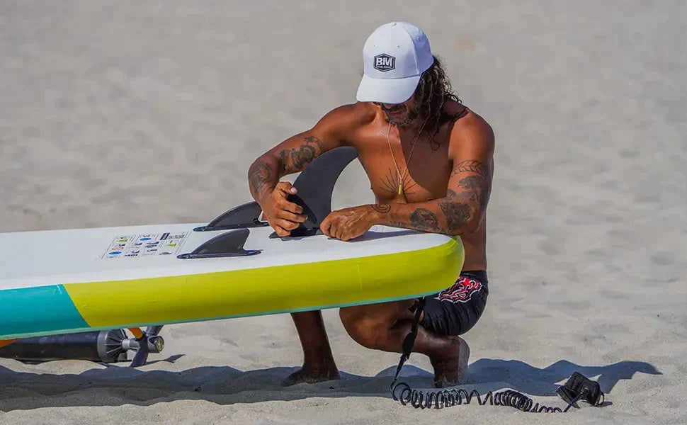 Man sitting on beach with surfboard, choosing tail fins for SUP