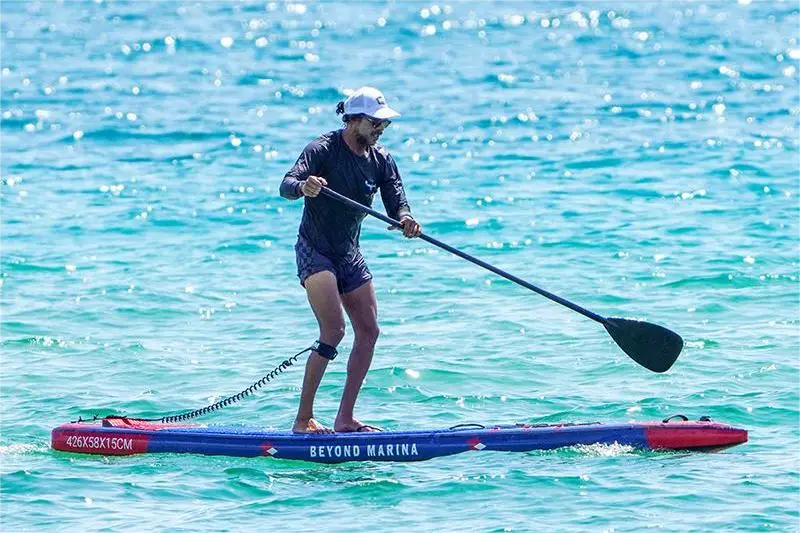 Man in long-sleeved shirt and shorts paddleboarding on colorful inflatable racing SUP