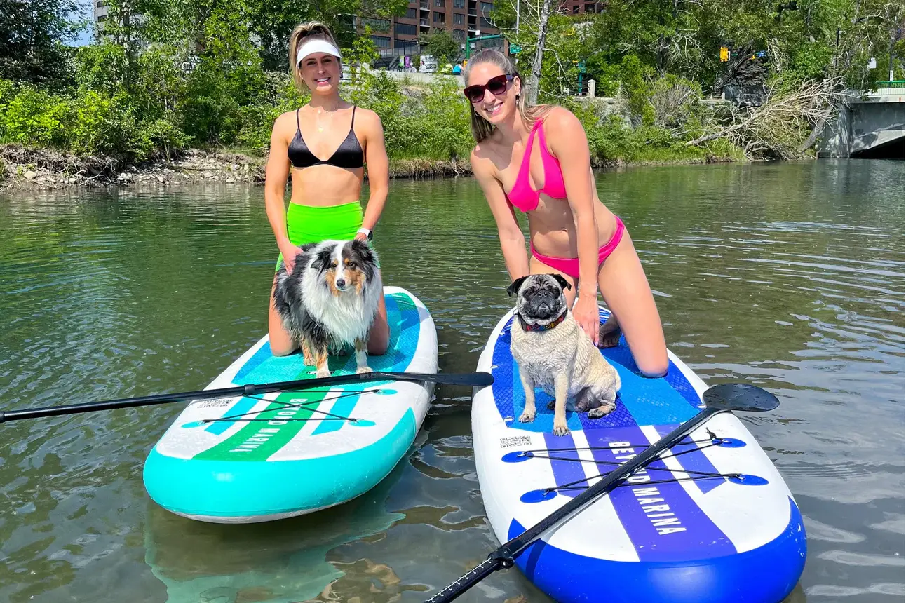 Two people walking on the beach with inflatable paddle boards ready for adventure.