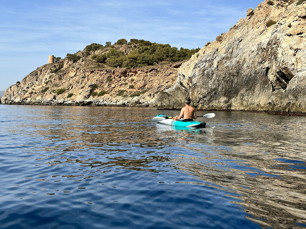 Person kayaking in calm water with a rocky cliff and greenery in the background