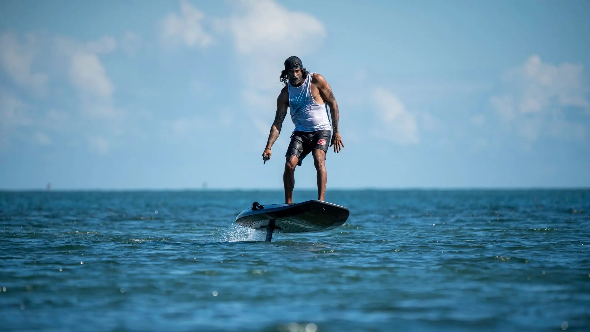 Person surfing on a wave with a clear blue sky and water, riding a sleek efoil surfboard