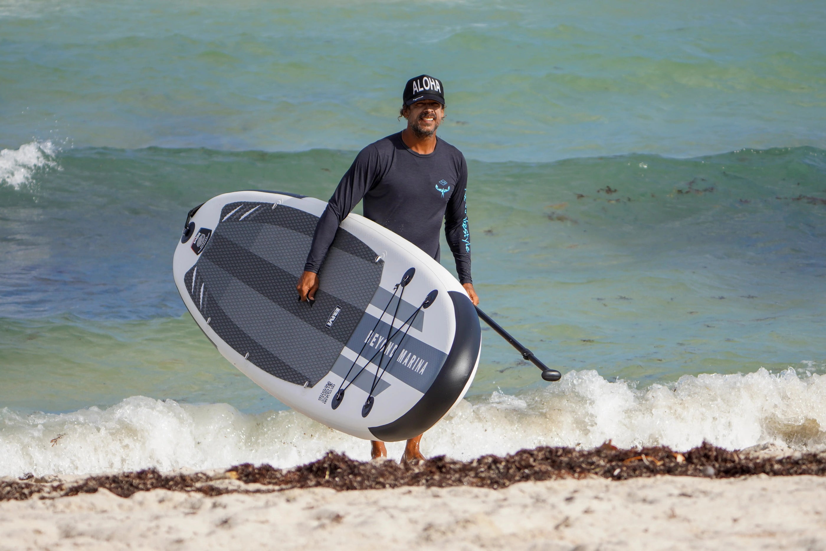Person holding a paddleboard on a beach with ocean waves in the background