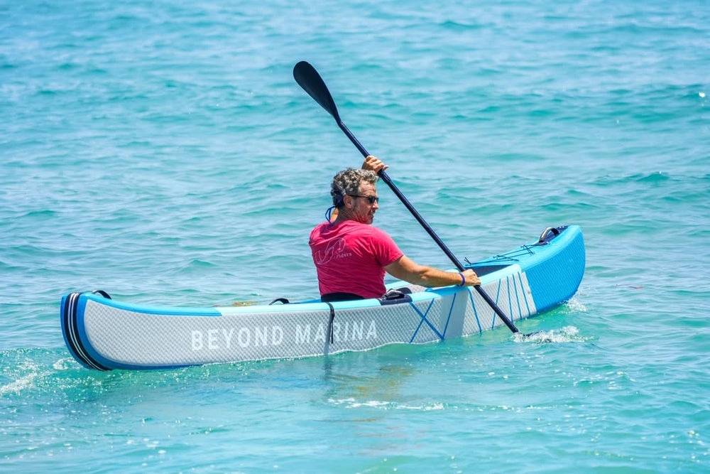 Person paddling a blue kayak with 'Beyond Marina' branding on a clear blue water background