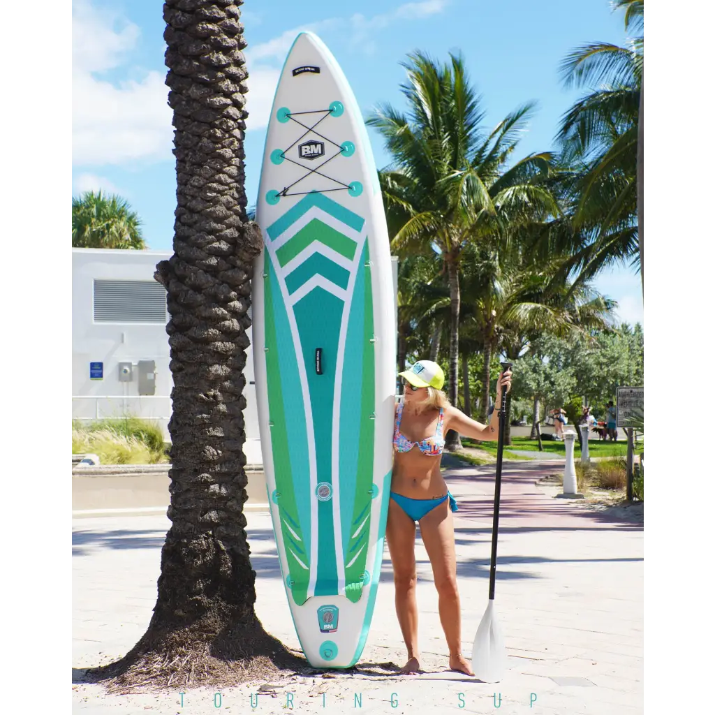 Woman standing next to a palm tree with Beyond Marina TOURING 11’6’ DISCOVERY DUAL AIR INFLATABLE PADDLE BOARD PACKAGE