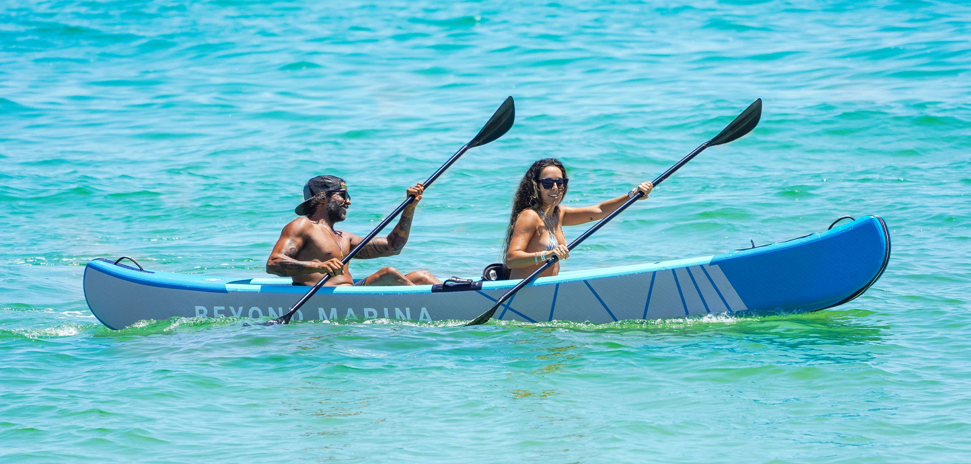 Two people paddling an inflatable kayak in clear blue water.