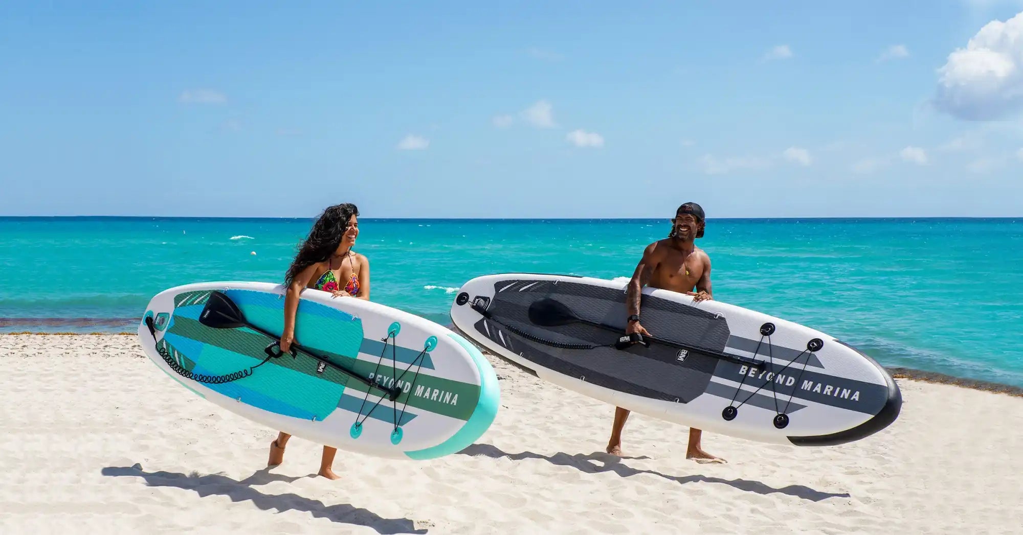 Two people carrying paddleboards.